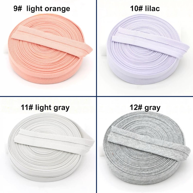 May include: Four spools of elastic ribbon in light orange, lilac, light gray, and gray. Each spool is labeled with a number and color name. The elastic is folded over and appears to be ready for use in sewing or crafting projects.