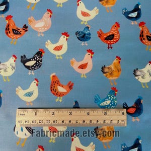 May include: A light blue fabric featuring a repeating pattern of chickens in various colors including white, orange, and dark blue. A wooden ruler is placed across the fabric, showing a measurement scale of 6 inches and 15 centimeters.