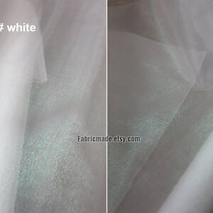 May include: Close-up of white fabric with a subtle sheen. The fabric is layered, creating depth and texture. The text "7# white" is visible in the upper left corner. The fabric appears to be lightweight and possibly used for apparel or decorative purposes.