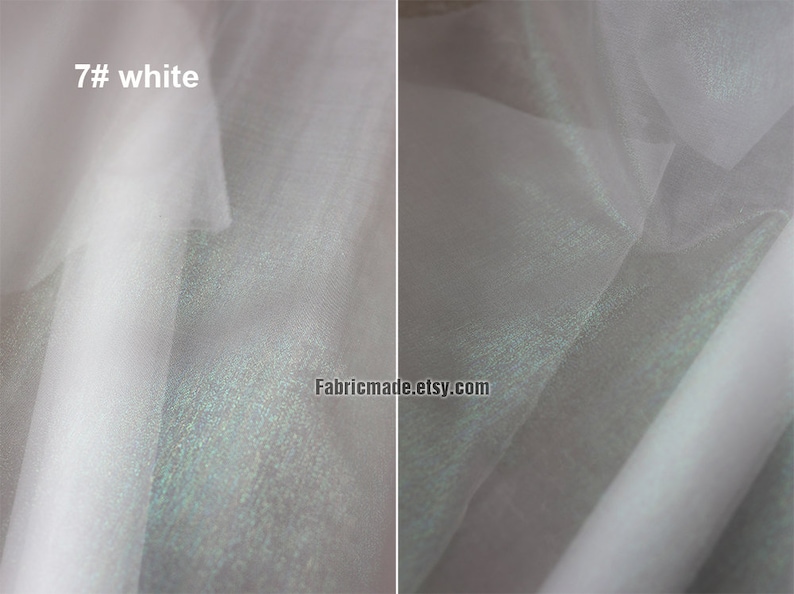 May include: Close-up of white fabric with a subtle sheen. The fabric is layered, creating depth and texture. The text "7# white" is visible in the upper left corner. The fabric appears to be lightweight and possibly used for apparel or decorative purposes.