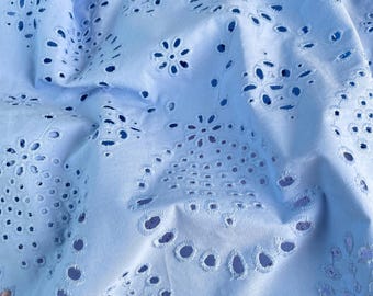 May include: Close-up of a light blue fabric with intricate eyelet embroidery. The fabric features a repeating pattern of floral and geometric cutouts, creating a delicate and airy texture. The website address fabricmade.etsy.com is visible.
