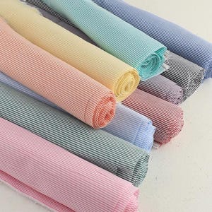 Op de afbeelding: Een verzameling opgerolde stoffen in verschillende kleuren, waaronder roze, groen, geel en blauw. Elke rol heeft een gestreept patroon. De stof lijkt katoen of een vergelijkbaar materiaal te zijn, geschikt voor naai- of knutselprojecten.