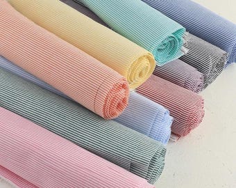 May include: A collection of rolled fabric bolts in various colors, including pink, green, yellow, and blue. Each bolt features a striped pattern. The fabric appears to be cotton or a similar material, suitable for sewing or crafting projects.