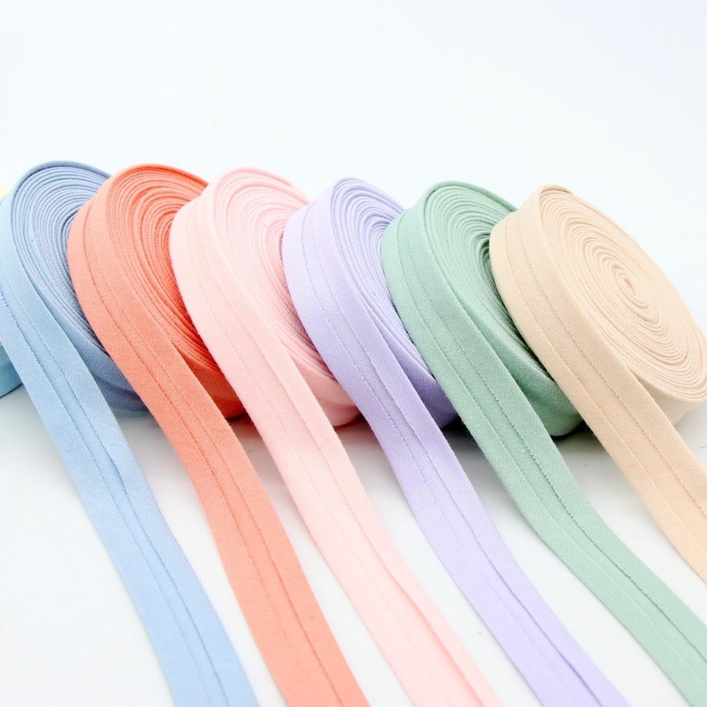 May include: A collection of colorful bias tape rolls in pastel shades. The colors include light blue, peach, pink, lavender, mint green, and beige. The bias tape is neatly rolled, showcasing the fabric's texture and color variations. Ideal for sewing and crafting projects.