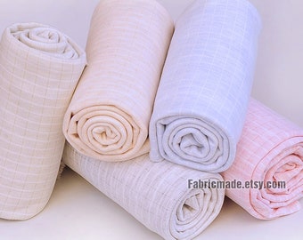 May include: Rolled fabric in various pastel colors, including beige, light pink, and pale blue. The fabric has a subtle grid pattern. The rolls are arranged in a visually appealing display, suggesting a textile product.