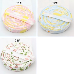 May include: Three rolls of patterned ribbon. One roll is pink with yellow and white designs, labeled "21#". Another is blue with yellow and white designs, labeled "22#". The third roll is white with a cherry and leaf pattern, labeled "23#".
