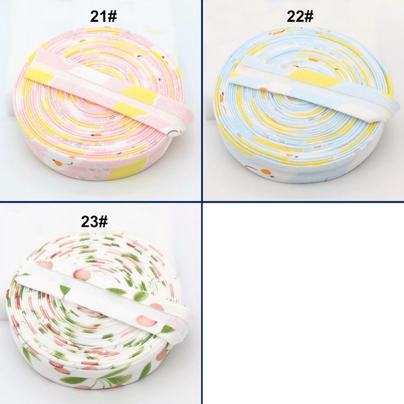 May include: Three rolls of patterned ribbon. One roll is pink with yellow and white designs, labeled "21#". Another is blue with yellow and white designs, labeled "22#". The third roll is white with a cherry and leaf pattern, labeled "23#".