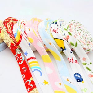 May include: A collection of colorful ribbons with various patterns, including floral, cartoon cars, and clouds. The ribbons are rolled up and displayed in a row, showcasing a variety of designs and colors.