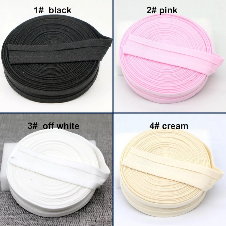 May include: Four spools of bias tape in various colors: black, pink, off-white, and cream. Each spool is labeled with a number and color name. The bias tape is neatly rolled, showcasing the different shades available for sewing and crafting projects.