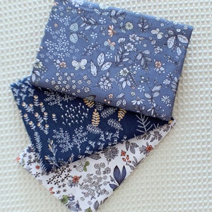 May include: Three fabric swatches featuring floral designs. The top swatch is a light blue fabric with a white floral pattern. The middle swatch is a dark blue fabric with a white floral pattern. The bottom swatch is a white fabric with a light blue and orange floral pattern.