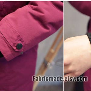Puede incluir: Primer plano de la manga de color burdeos de una chaqueta con un bot&oacute;n negro y un pu&ntilde;o de punto de canal&eacute; negro. El pu&ntilde;o est&aacute; doblado hacia atr&aacute;s para mostrar el forro interior.