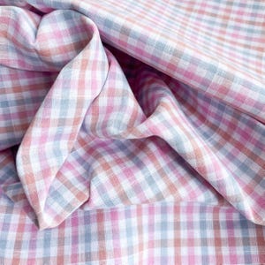 May include: Close-up of a fabric with a gingham pattern in shades of pink, white, gray, and peach. The fabric is folded and draped, showing the texture and pattern variations. The overall theme is textile design.