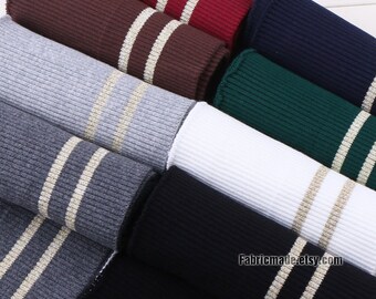 May include: A close-up of a stack of ribbed knit fabric with two gold stripes. The fabric is in various colors, including red, brown, gray, navy, green, white, and black.