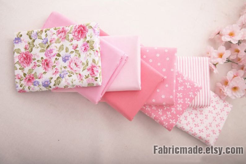 May include: A stack of pink and white fabric squares with floral and polka dot patterns. The fabric is soft and perfect for quilting, sewing, or crafting.