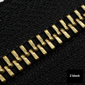 May include: Close-up of a black zipper with gold teeth. The zipper is made of a textured fabric.