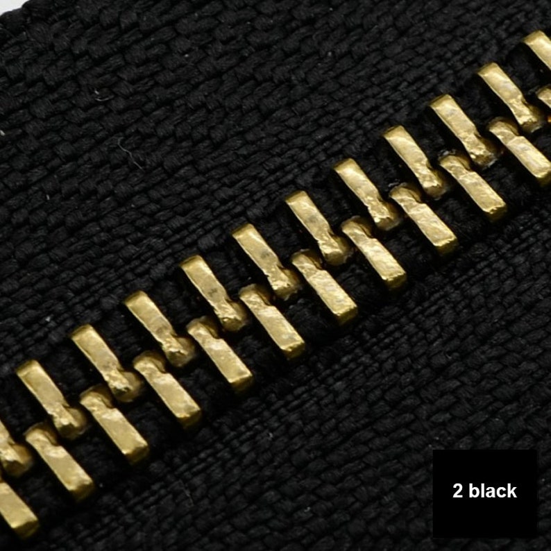 May include: Close-up of a black zipper with gold teeth. The zipper is made of a textured fabric.
