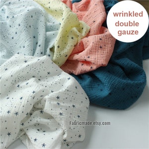 May include: A collection of wrinkled double gauze fabric in various colors, including white, light blue, yellow, peach, and teal. Each fabric is adorned with a pattern of small, dark blue stars. The fabric is soft and appears to be lightweight.