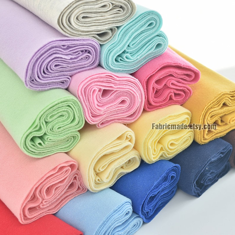Puede incluir: Una pila de tela enrollada en varios colores, incluyendo rojo, rosa, amarillo, verde, azul y gris. La tela est&aacute; dispuesta en forma de pir&aacute;mide, con la parte superior de la pir&aacute;mide siendo la tela gris. La tela est&aacute; toda enrollada apretadamente, y los extremos de los rollos son visibles. El texto "Fabricmade.etsy.com" es visible en la parte inferior derecha de la imagen.