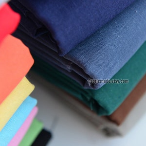 May include: A stack of fabric swatches in various colors, including orange, yellow, blue, green, and brown. The fabric is folded neatly and the top layer is a dark blue color. The text "Fabricmade.etsy.com" is visible on the bottom right corner of the image.
