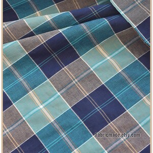 May include: Blue, teal, and beige plaid fabric. The fabric has a woven texture and is perfect for sewing projects.
