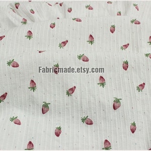 May include: White fabric with a repeating pattern of small red strawberries. The fabric has a subtle striped texture.