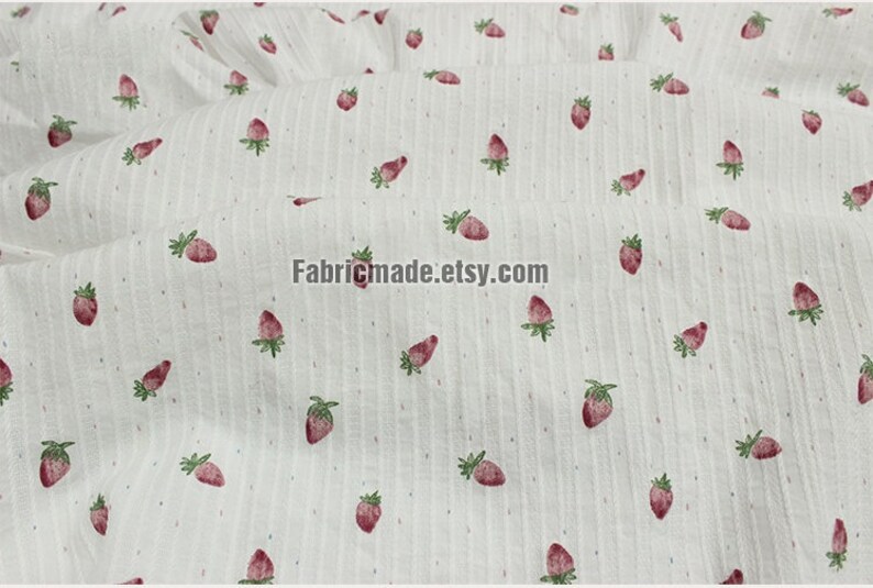 May include: White fabric with a repeating pattern of small red strawberries. The fabric has a subtle striped texture.