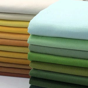 May include: A selection of corduroy fabric swatches in a variety of colours. The hues include cream, yellow, green, and brown. The fabric has a ribbed texture.