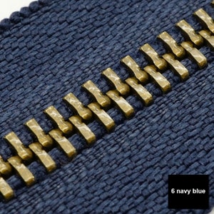 May include: Close-up of a navy blue zipper with gold metal teeth. The zipper is made of a woven fabric.