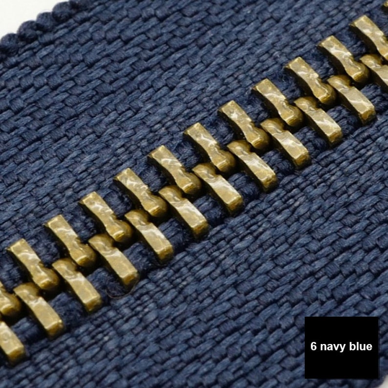 May include: Close-up of a navy blue zipper with gold metal teeth. The zipper is made of a woven fabric.