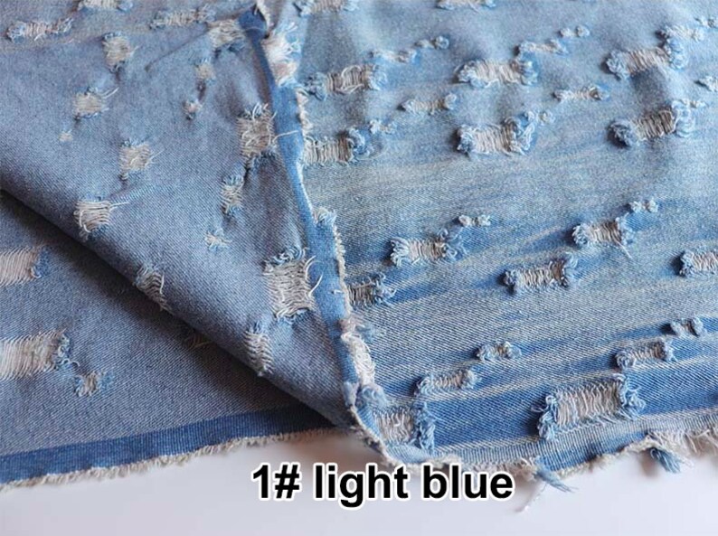 May include: Light blue denim fabric with a distressed, ripped look. The fabric has a horizontal pattern of small holes and frayed edges.