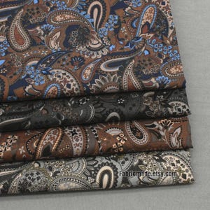 May include: Four pieces of fabric with a paisley pattern in shades of brown, blue, and gray. The fabric is folded in a stack.