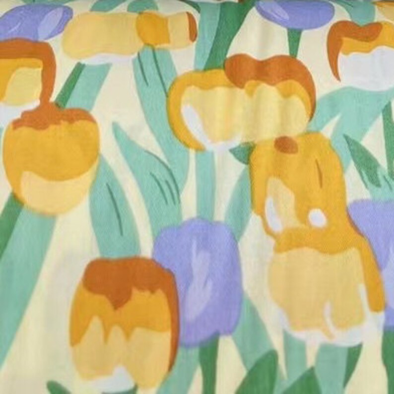 May include: A yellow fabric with a repeating pattern of stylized flowers in shades of yellow, orange, and purple. The flowers are outlined in green and set against a light yellow background.