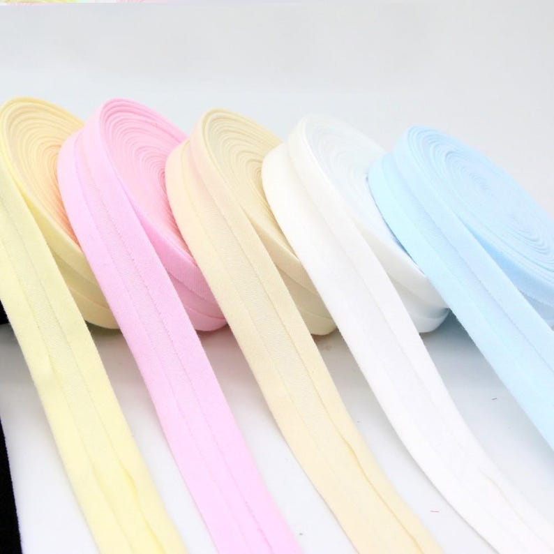 May include: A collection of colorful elastic ribbon rolls in pastel shades. The ribbons are in shades of yellow, pink, cream, white, and light blue. The ribbons are neatly coiled and ready for use in various craft projects.