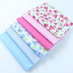 May include: A stack of six fabric squares in various patterns. The top square is white with pink flowers, the second is pink with white gingham, the third is white with blue flowers, the fourth is blue with white gingham, the fifth is light blue solid, and the bottom is white with blue gingham.
