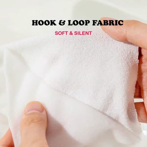 May include: A white hook and loop fabric with a soft, textured surface. The text HOOK & LOOP FABRIC is printed in black, and the text SOFT & SILENT is printed in red. The material is shown being held and pulled to demonstrate its texture.