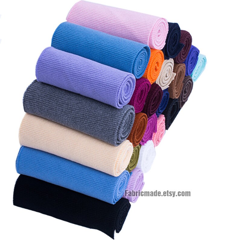Op de afbeelding: Een stapel gerolde gebreide stof in verschillende kleuren, waaronder roze, blauw, paars, grijs, beige en zwart. De stof is in een verspringend patroon gerangschikt, met de bovenste rol roze en de onderste rol zwart. De stof wordt waarschijnlijk gebruikt voor naai- of knutselprojecten. De tekst "Fabricmade.etsy.com" is zichtbaar onderaan de afbeelding.