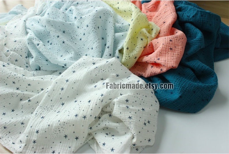 May include: Assortment of soft, textured fabric in various colors, including white, light blue, yellow, peach, and teal. Each fabric is adorned with a pattern of small, dark blue stars. The Etsy shop name "Fabricmade.etsy.com" is visible.