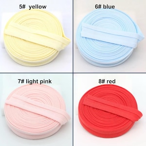 May include: Four spools of fabric trim in yellow, blue, light pink, and red. Each spool is labeled with a number and color name. The trim is folded over and appears to be made of a soft, flexible material.