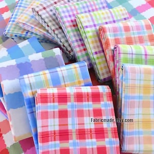 Puede incluir: Una pila de cuadrados de tela de cuadros coloridos en varios tonos de azul, rosa, amarillo y verde. La tela está dispuesta en forma de abanico, con el cuadrado inferior siendo un cuadro rojo y blanco.