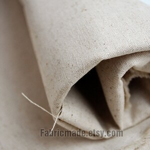 May include: Close-up of a natural, off-white, woven fabric rolled up. The fabric has a slightly rough texture and a subtle sheen. The fabric is unbleached and has a natural, rustic look. The text "Fabricmade.etsy.com" is visible in the lower right corner of the image.