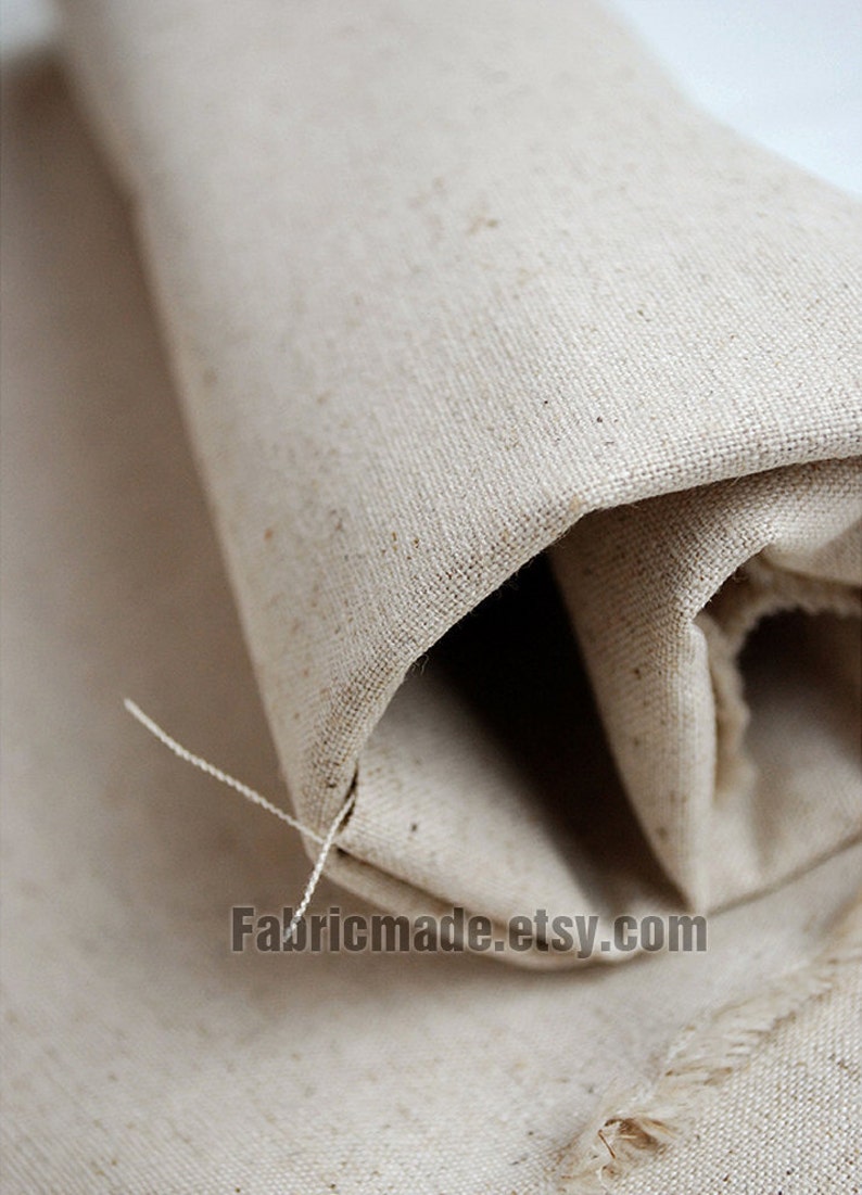 May include: Close-up of a natural, off-white, woven fabric rolled up. The fabric has a slightly rough texture and a subtle sheen. The fabric is unbleached and has a natural, rustic look. The text "Fabricmade.etsy.com" is visible in the lower right corner of the image.