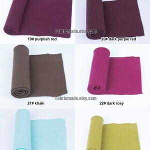 Op de afbeelding: Zes rollen geribbelde brei in verschillende kleuren, waaronder paarsachtig rood, donkerpaarsrood, kaki, donkerroze, lichtblauw en geelgroen. Fabricmade.etsy.com is afgedrukt op de afbeelding.