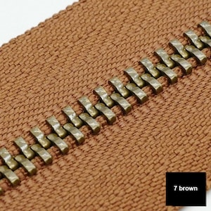 May include: Close-up of a brown zipper tape with a row of gold metal teeth. The zipper tape has a woven texture. The text "7 brown" is visible in the lower right corner of the image.