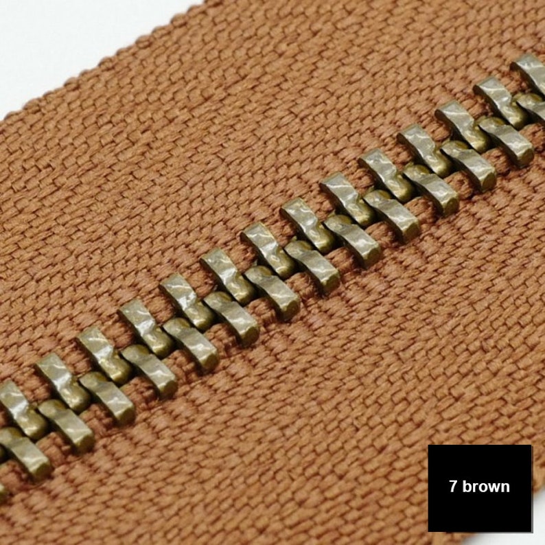 May include: Close-up of a brown zipper tape with a row of gold metal teeth. The zipper tape has a woven texture. The text "7 brown" is visible in the lower right corner of the image.