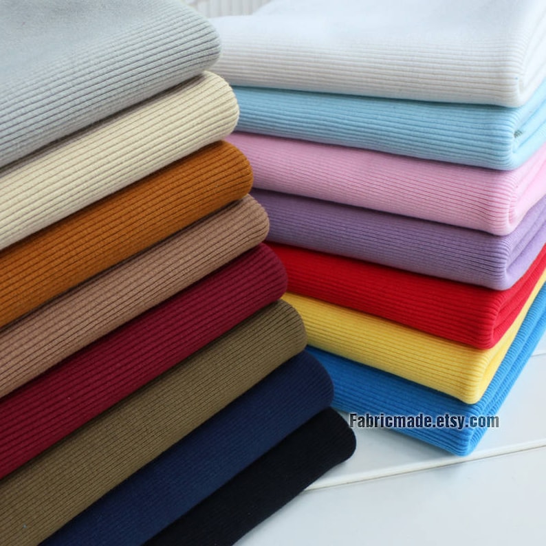 Puede incluir: Una pila de 12 telas de punto de canal&eacute; de diferentes colores. Los colores son gris claro, beige, marr&oacute;n, tostado, burdeos, verde oliva, azul marino, negro, azul claro, rosa, lavanda y rojo. La tela est&aacute; doblada cuidadosamente y apilada sobre una superficie de madera. El texto "Fabricmade.etsy.com" es visible en la parte inferior de la imagen.