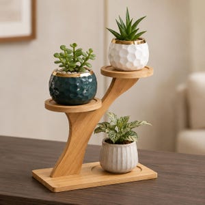 Op de afbeelding: Een gelaagde bamboe plantenstandaard met drie niveaus en drie keramische potten. De bovenste pot is wit met een honingraatstructuur, de middelste is donkerblauwgroen met een honingraatstructuur en de onderste is een lichtgrijze geribbelde pot.