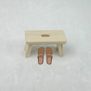 May include: A wooden stool with a rectangular top and four legs. Two brown leather sandals are placed on top of the stool.