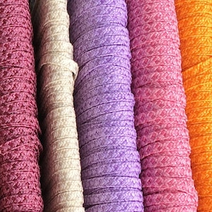 Könnte beinhalten: Eine Auswahl an bunten gemusterten Borten, Spulen mit Band und Schnüren in verschiedenen Farben und Texturen.