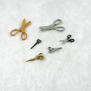 May include: A set of six miniature scissors in gold, silver, and black. The scissors are arranged on a white surface.