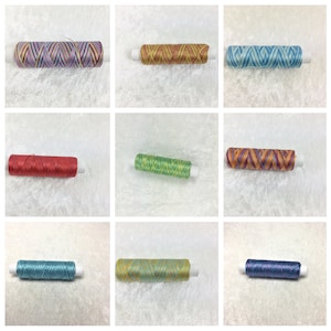 Könnte beinhalten: Neun Spulen mit buntem Stickgarn mit verschiedenen Mustern. Das Garn ist auf weiße Spulen gewickelt.